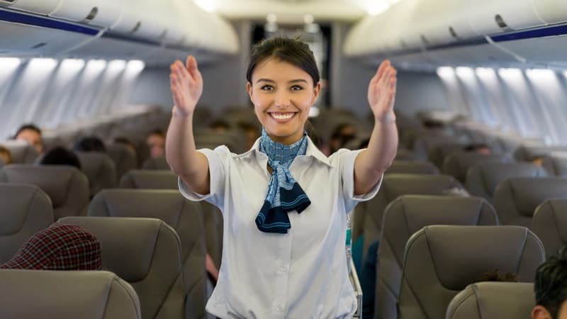 Hôtesse de l'air souriante accueillant les passagers, bras ouverts, dans un avion.